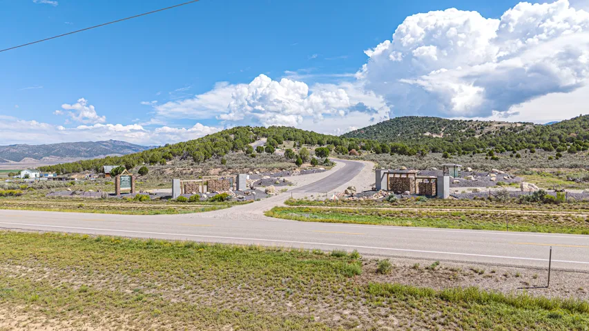 Roadside entrance with stone and wood-finish structures, leading to a paved ascending road