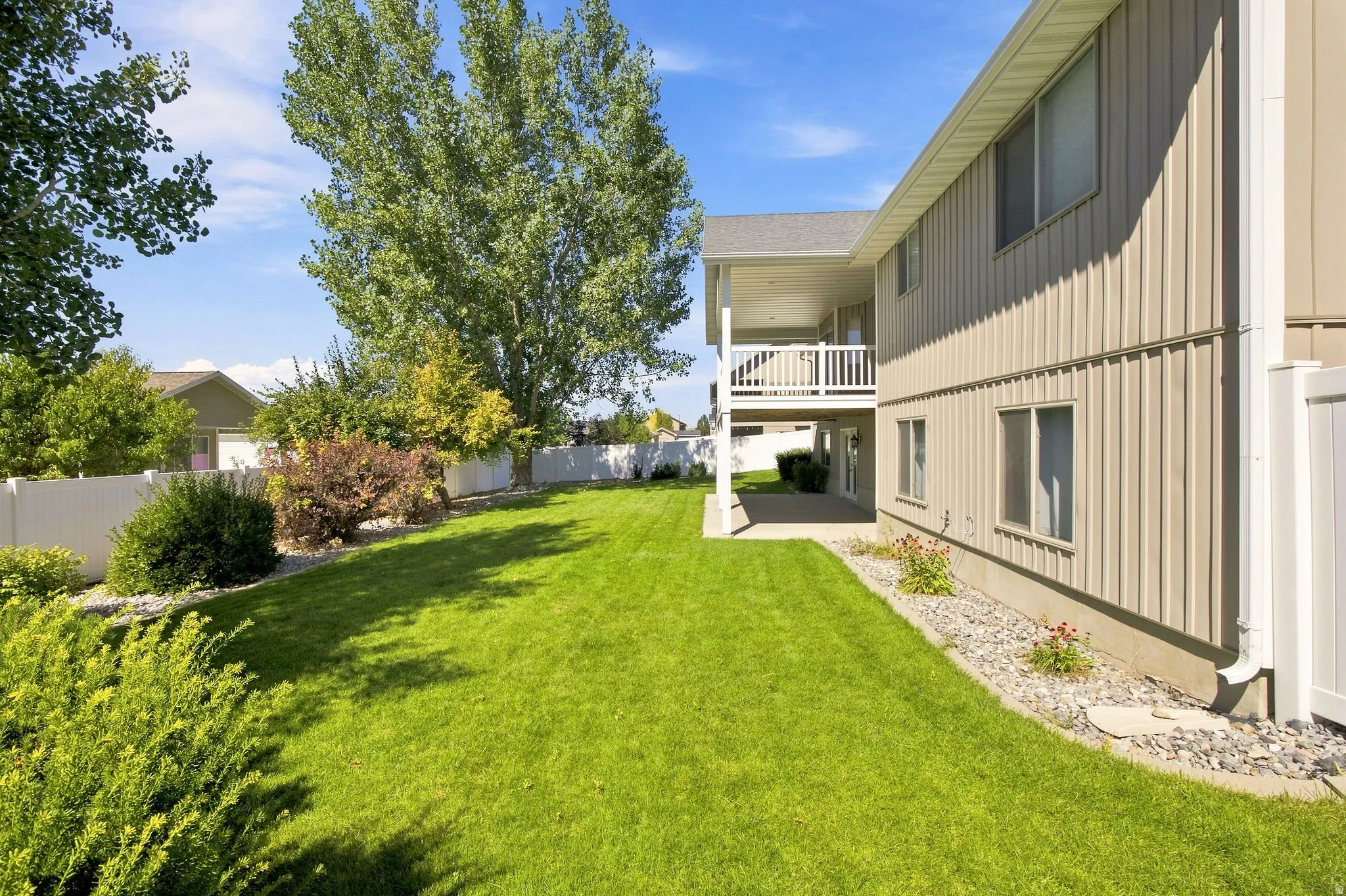 Expansive green lawn, mature trees, white privacy fencing, covered patio, and upper-level balcony