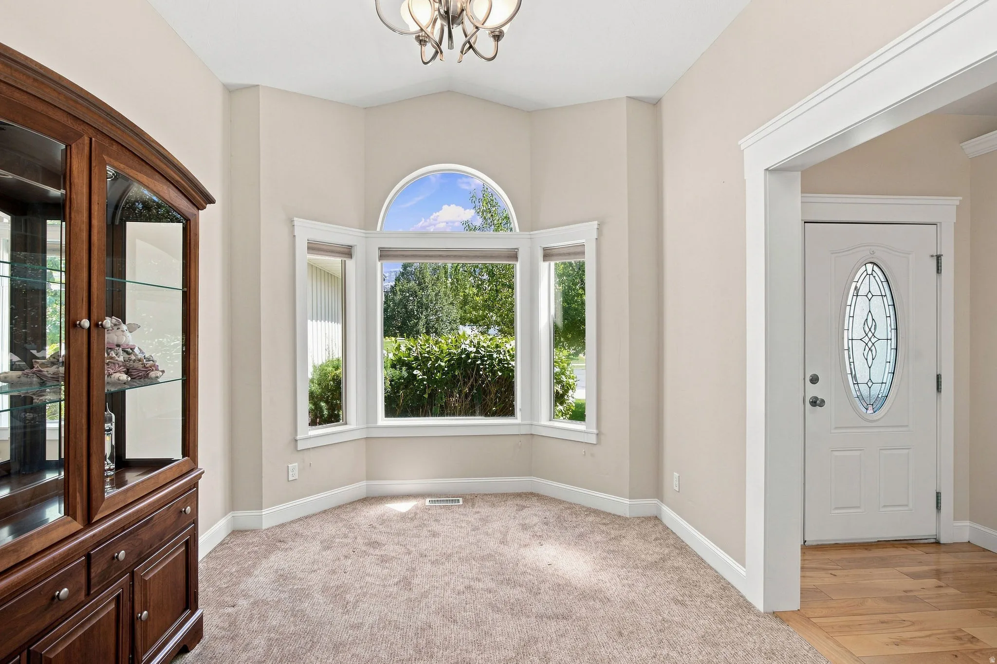 Bay window with arched transom, chandelier lighting, and a front entry door with leaded glass insert. Carpeted floors.