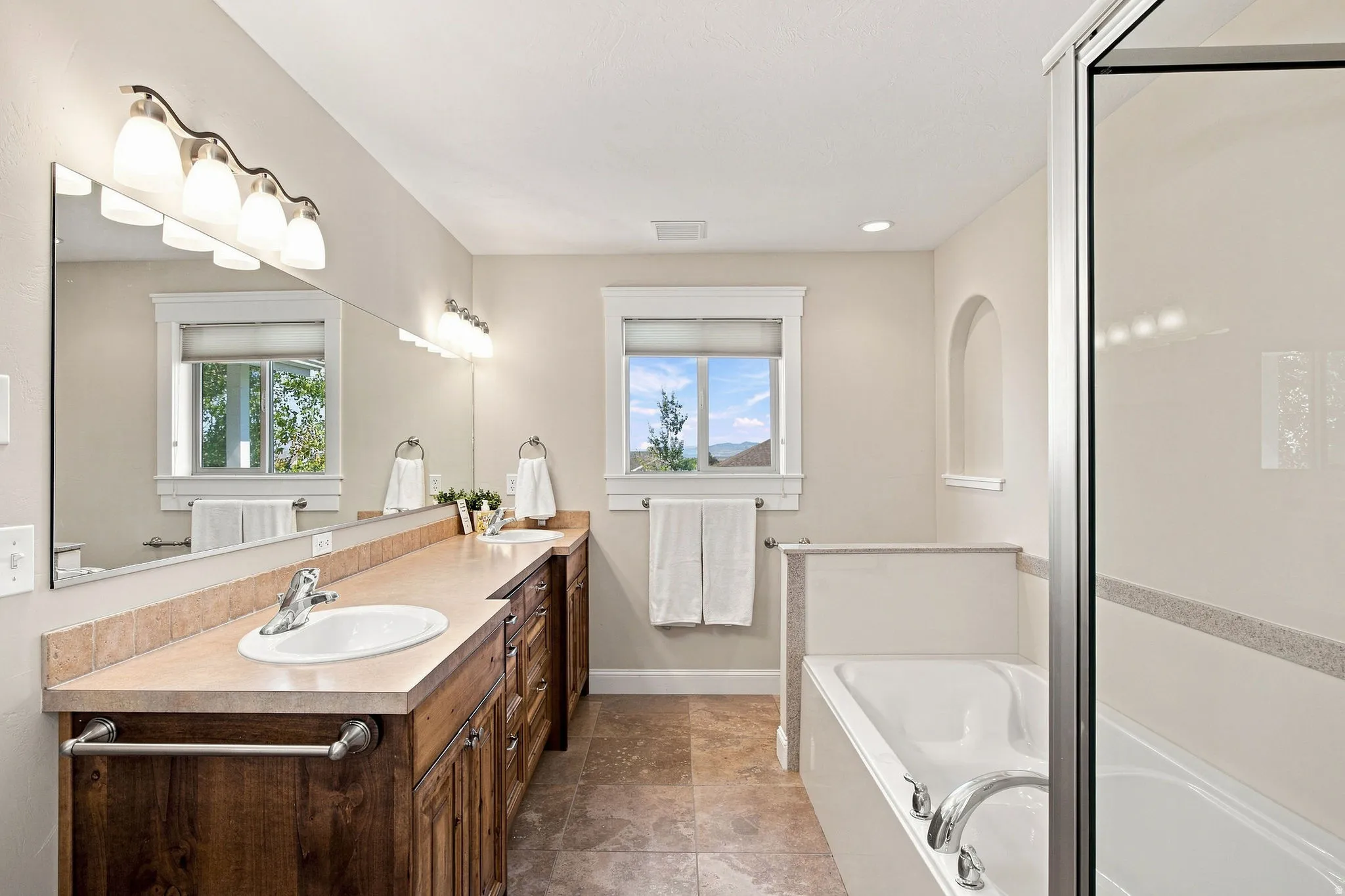 Primary ensuite. Dual vanity with wood-finish cabinetry, a large built-in mirror, and sconce lighting