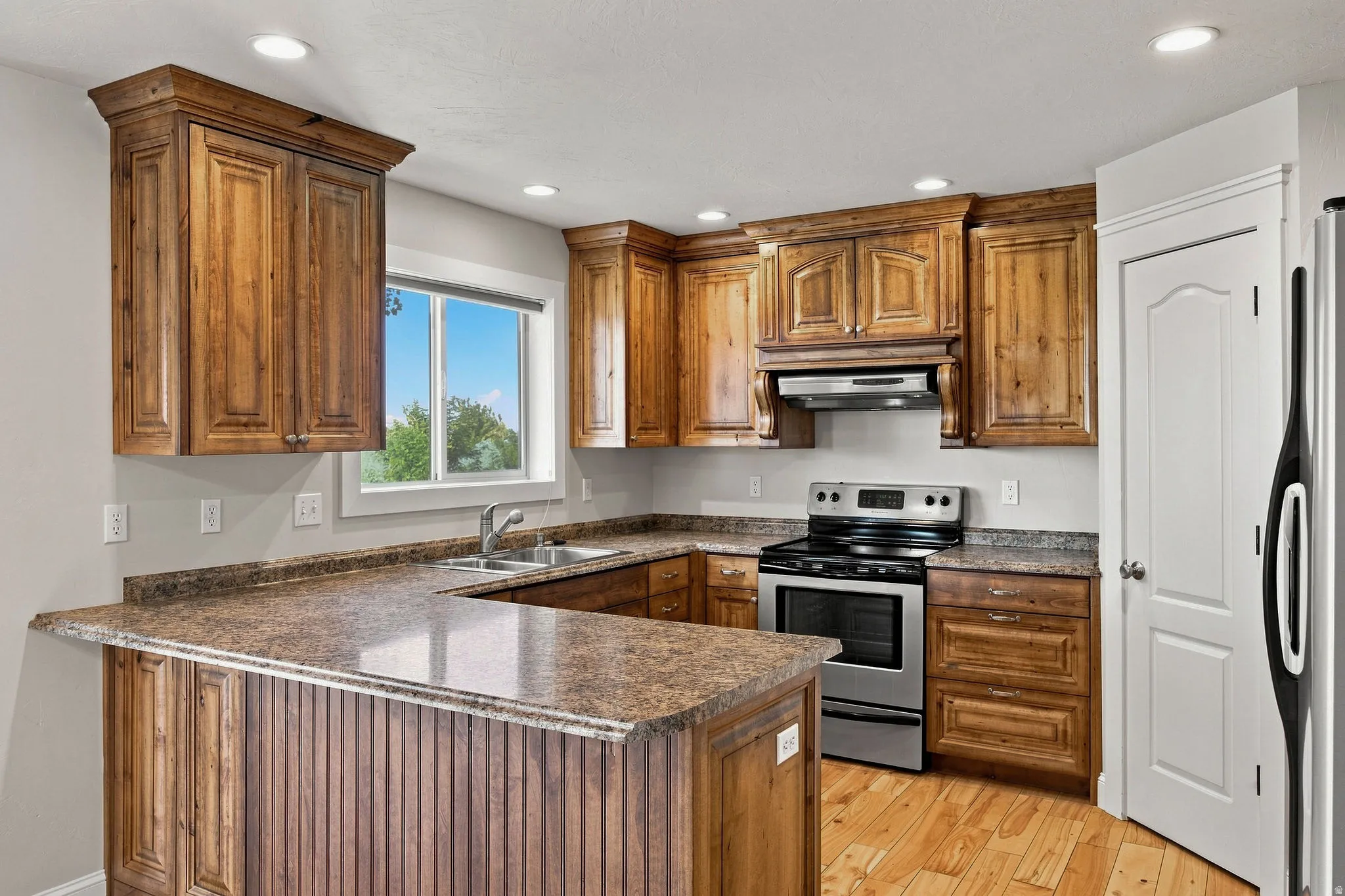 Wood-finish cabinetry with crown molding, stainless steel range and hood, dual basin sink, recessed ceiling lights, and wood-finish flooring