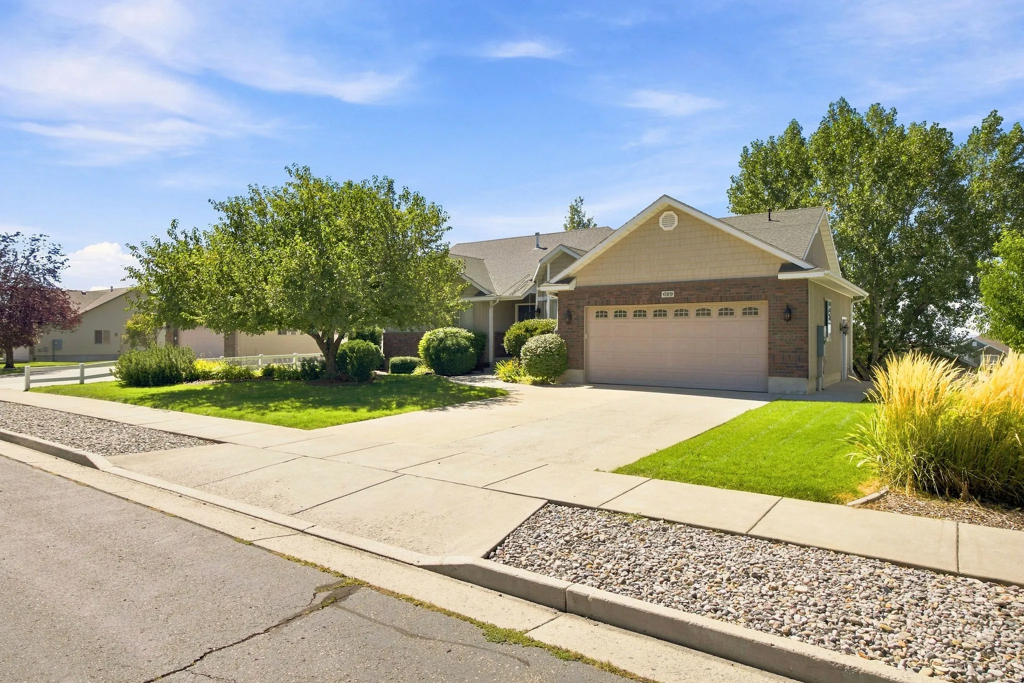 Brick and siding exterior with an attached garage, concrete driveway, and landscaped front yard featuring mature trees and shrubs