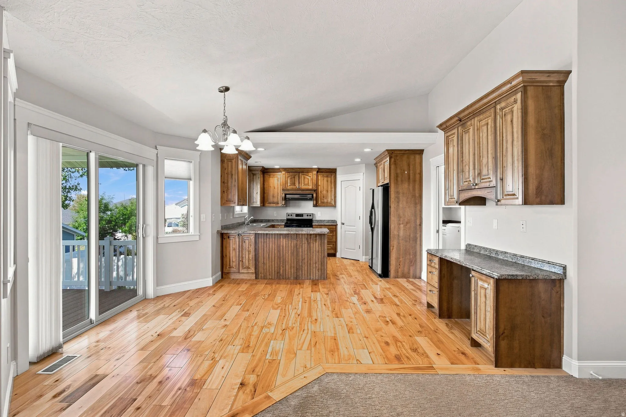 Light wood-finish flooring, sliding glass door, recessed lighting, wood cabinetry, and a vaulted ceiling