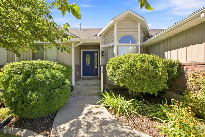 Exterior featuring a blue entry door, an arched window, a gabled roofline, and established landscaping