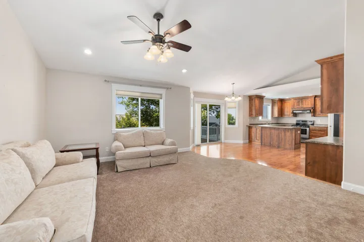 Open-concept living space featuring a ceiling fan with integrated lighting, recessed lighting, and a kitchen with carpet, wood cabinetry and granite countertops