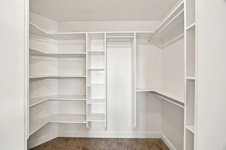 Primary bedroom closet. Custom built-in white shelving system featuring multiple storage levels and hanging rods