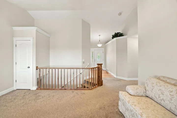 Vaulted ceiling, carpeted flooring, wood staircase, white interior door, and pendant lighting