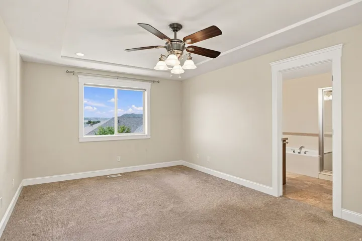 Primary bedroom. Tray ceiling with recessed lighting, ceiling fan, large window, and broad doorway