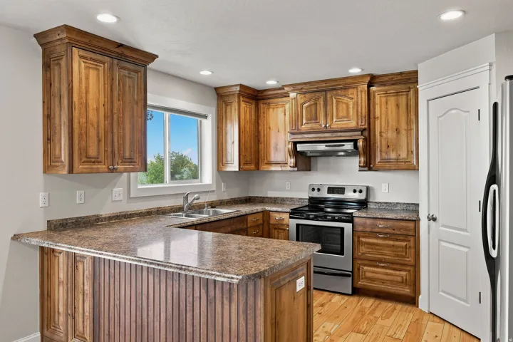 Wood-finish cabinetry with crown molding, stainless steel range and hood, dual basin sink, recessed ceiling lights, and wood-finish flooring