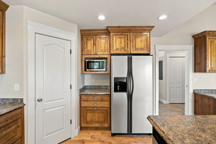 Kitchen featuring wood-finish cabinetry, granite countertops, stainless steel side-by-side refrigerator, built-in microwave, and wood-finish flooring