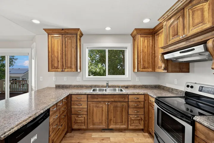 Kitchen featuring wood-finish cabinetry, stone-finish countertops, stainless steel appliances, a double basin sink, and recessed lighting