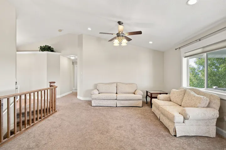Carpeted living area with vaulted ceilings, recessed lighting, a ceiling fan, and a wood-finish staircase railing
