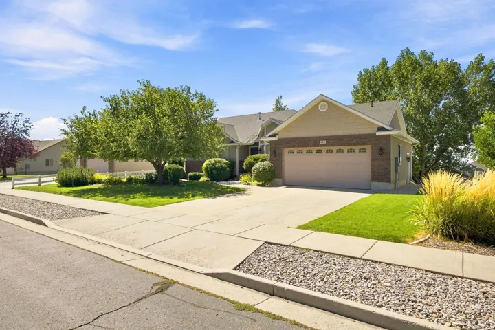 Brick and siding exterior with an attached garage, concrete driveway, and landscaped front yard featuring mature trees and shrubs