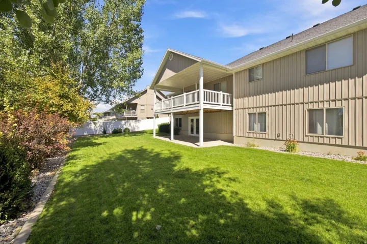 Expansive backyard featuring a manicured lawn, an upper-level covered balcony, and a lower-level covered patio with French doors