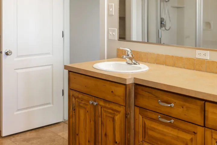 Primary ensuite. Wood-finish vanity with an integrated sink, polished chrome faucet, and tiled backsplash