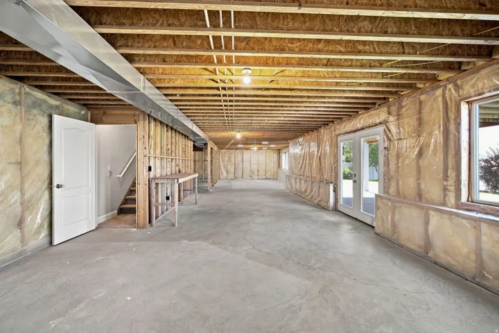 Unfinished basement with exposed ceiling joists, concrete flooring, and multiple windows