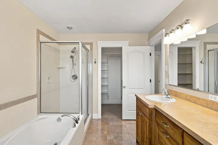 Primary ensuite. Dual-function bathtub with an integrated shower, wood-finish vanity with a rectangular sink, large wall-mounted mirror, and tile flooring