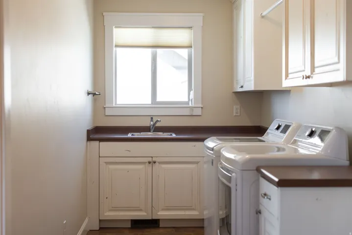 Laundry area with white cabinetry, a utility sink, and a window with a roller shade