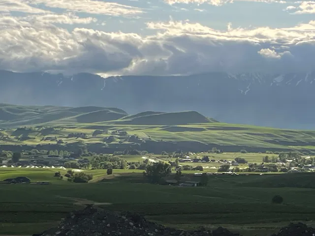 Expansive green hills, distant snow-capped mountains, and scattered residential structures