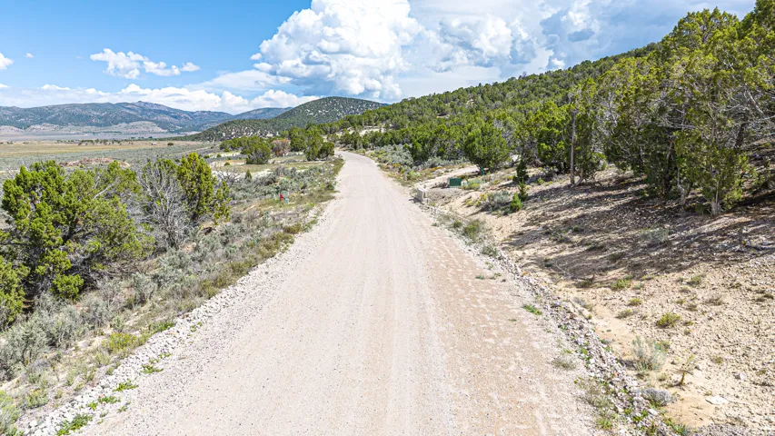 Gravel road surrounded by natural landscaping, distant mountains, and partially cloudy sky