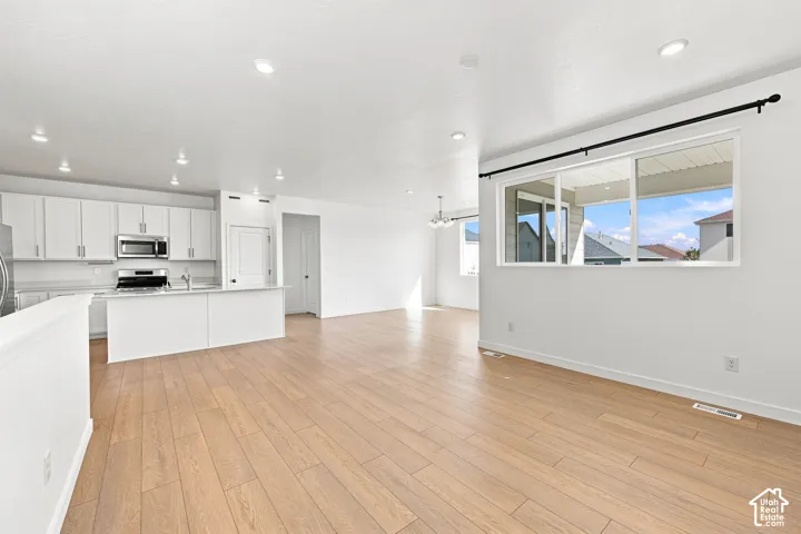 Open-concept living space featuring wood-finish flooring, recessed lighting, white cabinetry, stainless steel appliances, and a kitchen island
