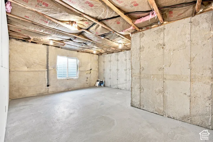 Unfinished basement featuring concrete flooring, exposed ceiling joists, insulated walls, and a window