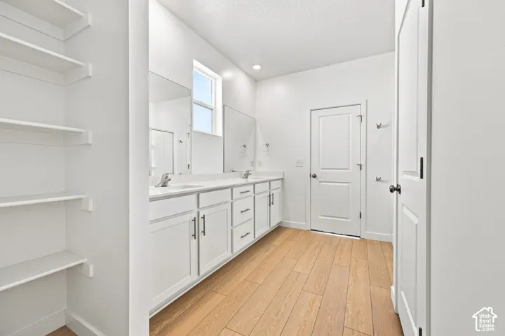 Master bathroom: Dual vanity with white cabinetry, wood-finish flooring, built-in shelving, white walls, and a window