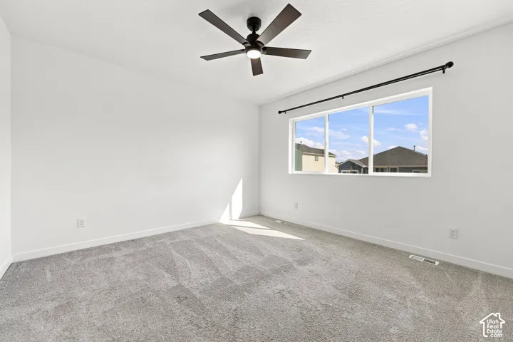 Master bedroom: Expansive room featuring light gray carpeting, a large three-panel window, a ceiling fan with integrated lighting, and crisp white walls