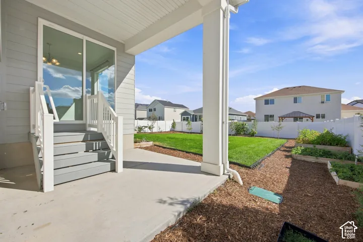 Concrete patio with covered area, leading to a grassy yard featuring raised garden beds and a privacy fence