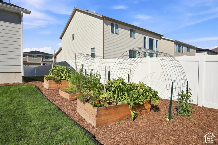 Expansive backyard featuring a manicured lawn, raised garden beds, and a white privacy fence