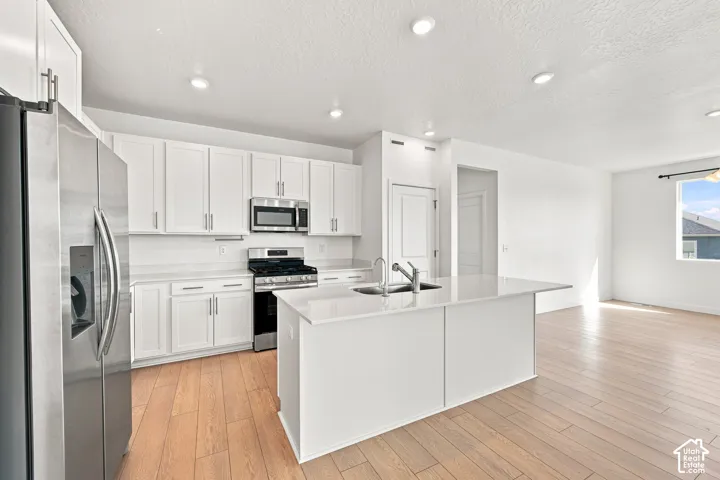 Kitchen featuring white cabinetry, stainless steel appliances, a center island with sink, white countertops, and wood-finish flooring