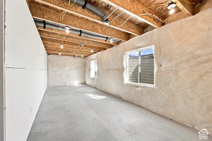 Unfinished basement with exposed ceiling joists, concrete flooring, and multiple windows