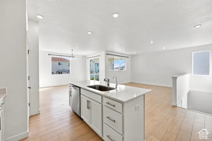 Open-concept living area with wood-finish flooring, recessed lighting, and a kitchen island featuring a stainless steel sink