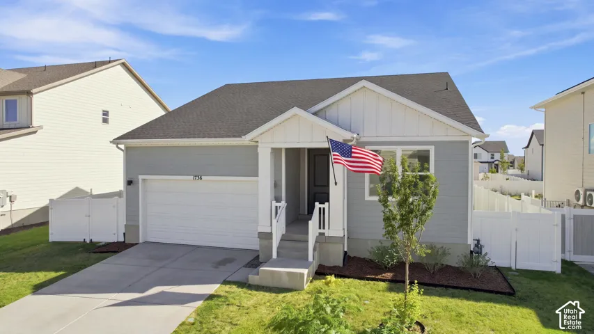 Room for RV pad on side of home: Single-story residence featuring light gray siding, a white front porch with railings, and an attached two-car garage