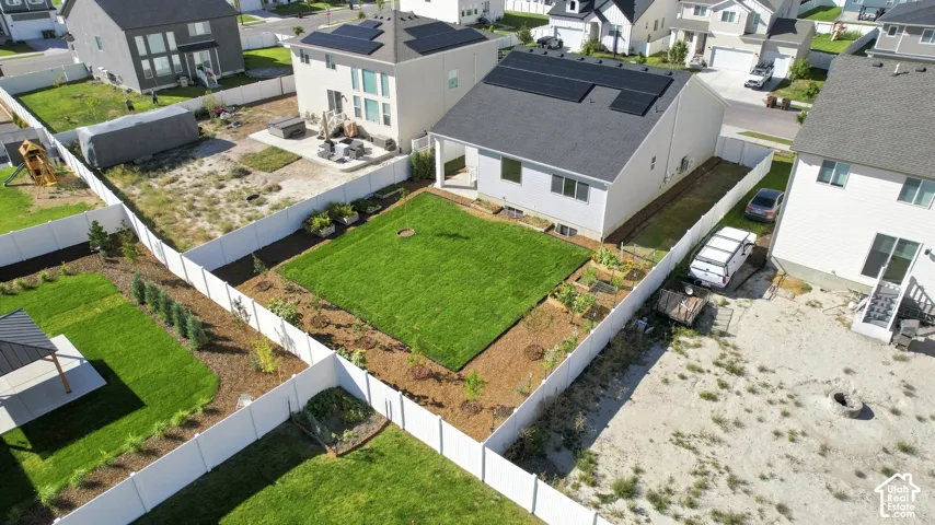 Manicured lawn with surrounding garden beds, white privacy fencing, and a covered back patio