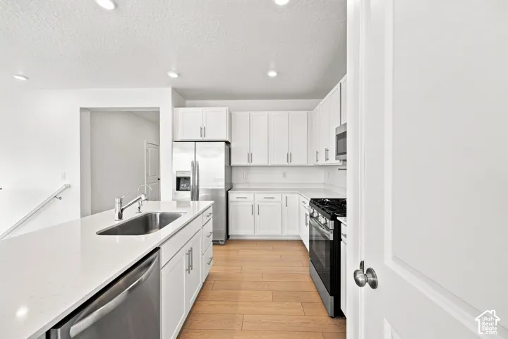 Kitchen featuring white cabinetry, light countertops, wood-finish flooring, stainless steel appliances, and an island with an undermount sink