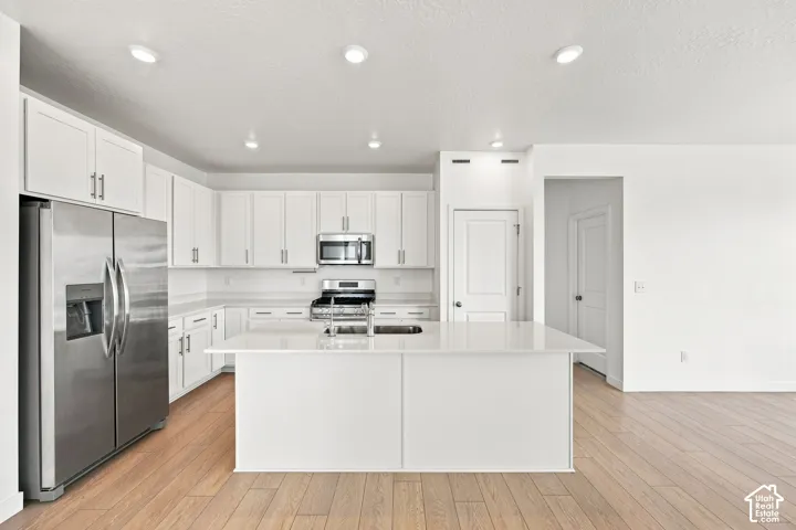 Kitchen featuring white cabinetry, stainless steel appliances, a center island with sink, light-toned wood-finish flooring, and recessed lighting