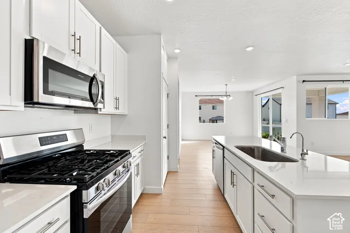 Kitchen featuring an island with an integrated sink, stainless steel appliances, white cabinetry, recessed lighting, and wood-finish flooring