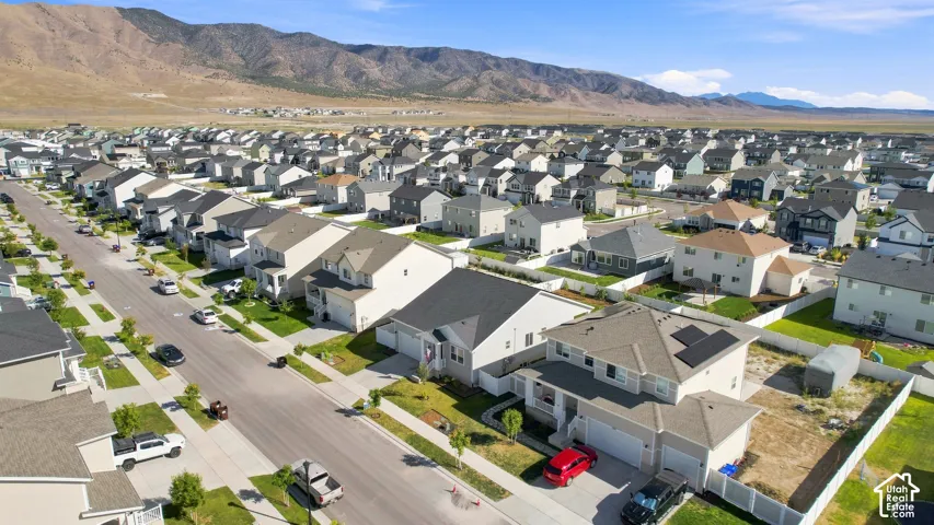 Residential street with uniform lot sizes and mature landscaping, featuring two-story homes with attached garages, light-colored exteriors, and a mountain backdrop