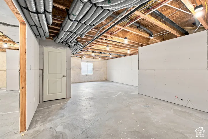 Unfinished basement featuring exposed wood joists, concrete flooring, and partial drywall installation