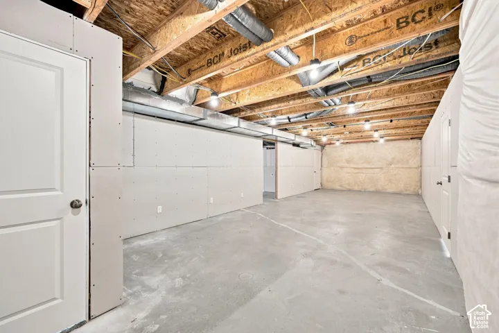 Unfinished basement with exposed ceiling joists, concrete flooring, recessed lighting, and framed walls ready for customization