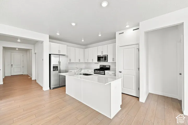 Open-concept kitchen featuring an island, stainless steel appliances, white cabinetry, and recessed lighting