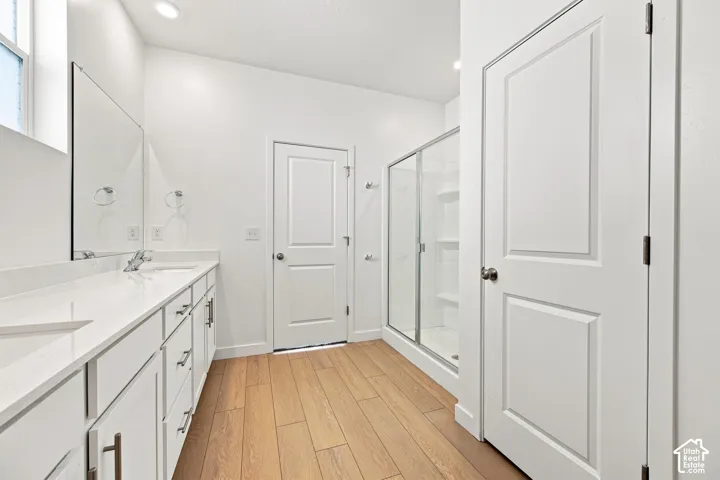 Master bathroom: Dual sink vanity with white cabinetry, wood-finish flooring, recessed lighting, and a glass-enclosed shower