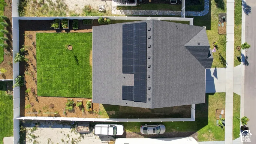Gable roof with solar panel array, fenced backyard, manicured lawn, and raised garden beds