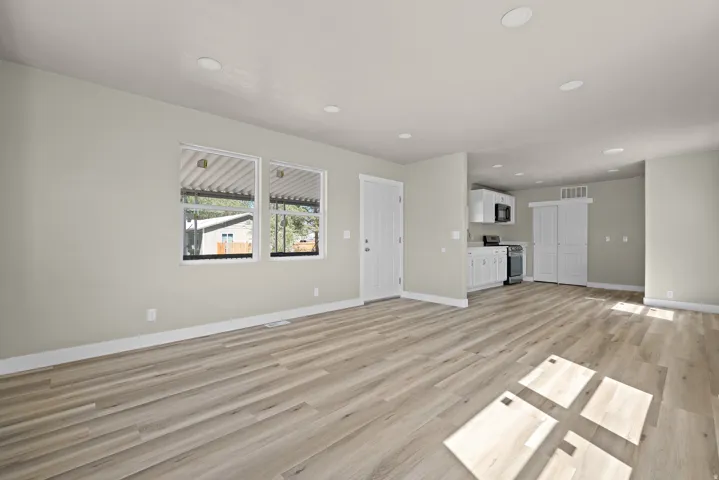 Wood-finish flooring, recessed lighting, white kitchen cabinetry, stainless steel appliances, and a white paneled door