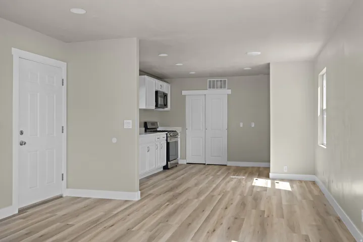Wood-finish flooring, recessed lighting, white shaker-style cabinetry, stainless steel appliances, and white trim throughout