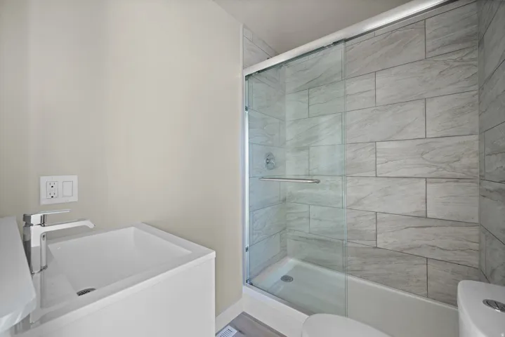 Wall-mounted vanity with a rectangular sink and chrome faucet, glass-enclosed shower with tile surround, and a white toilet