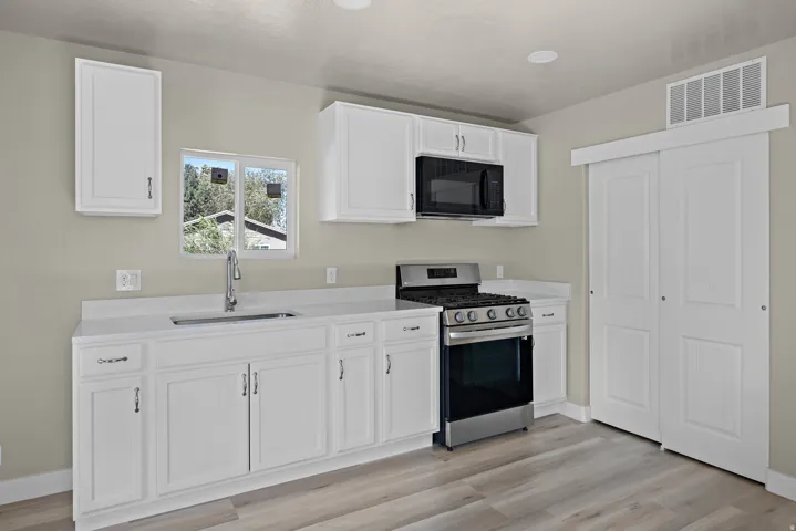 White cabinetry and countertops, stainless steel appliances, wood-finish flooring, and recessed lighting
