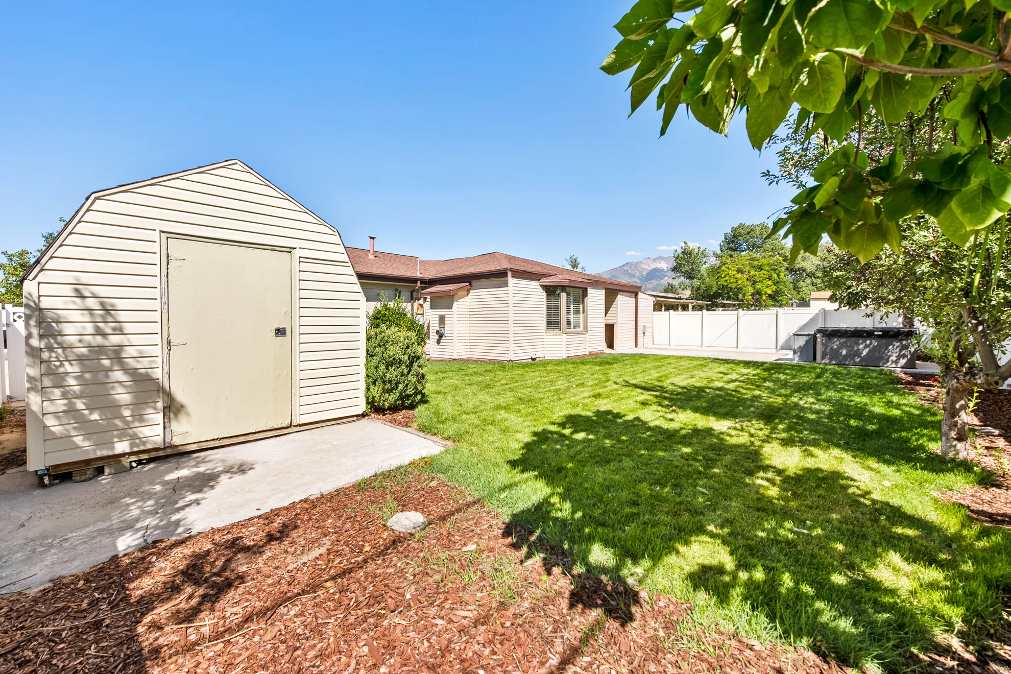 Expansive backyard featuring a manicured lawn, established trees, and a storage shed with a concrete pad