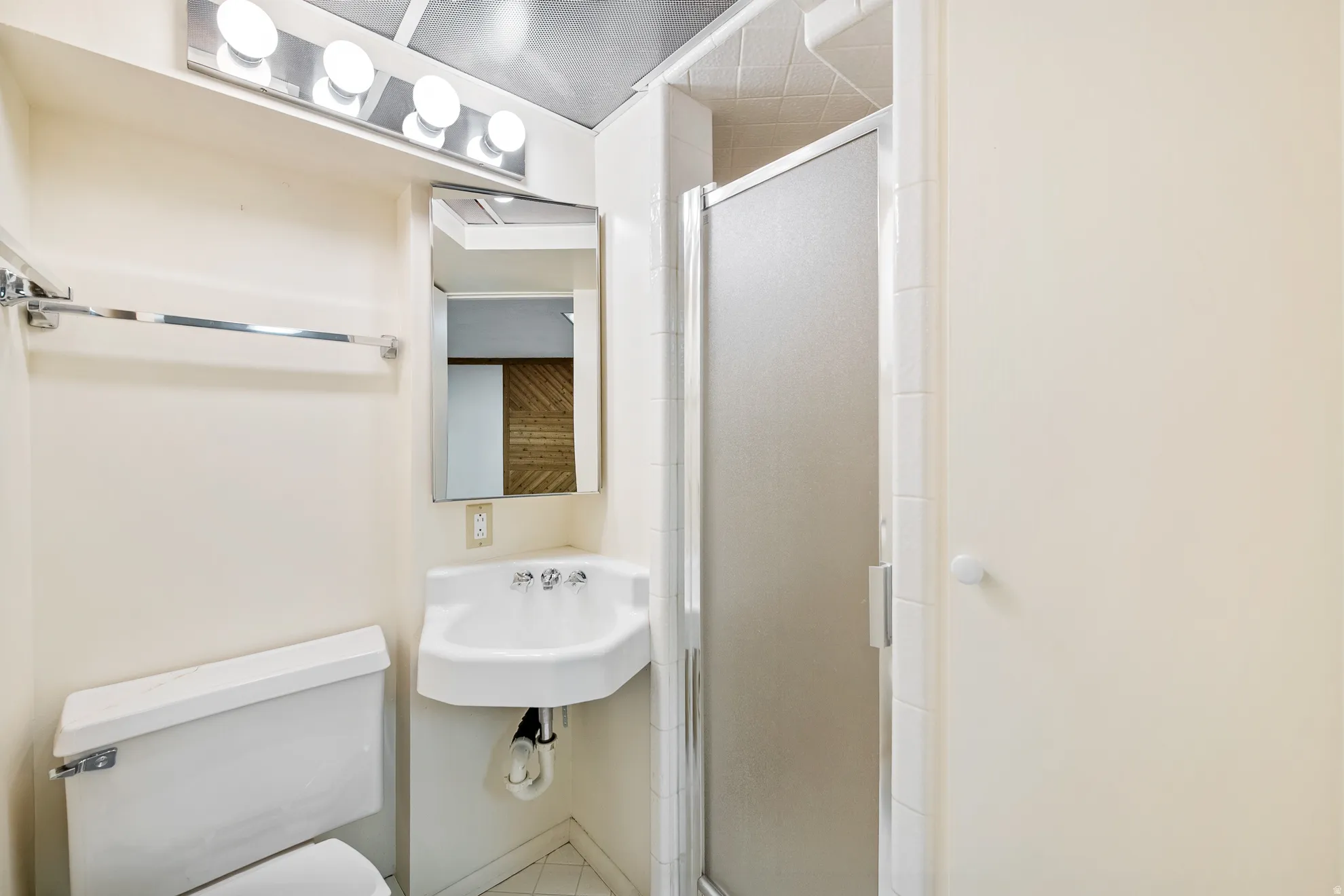 Bathroom featuring a shower enclosure with a frosted glass door, a wall-mounted sink, and a mirrored medicine cabinet
